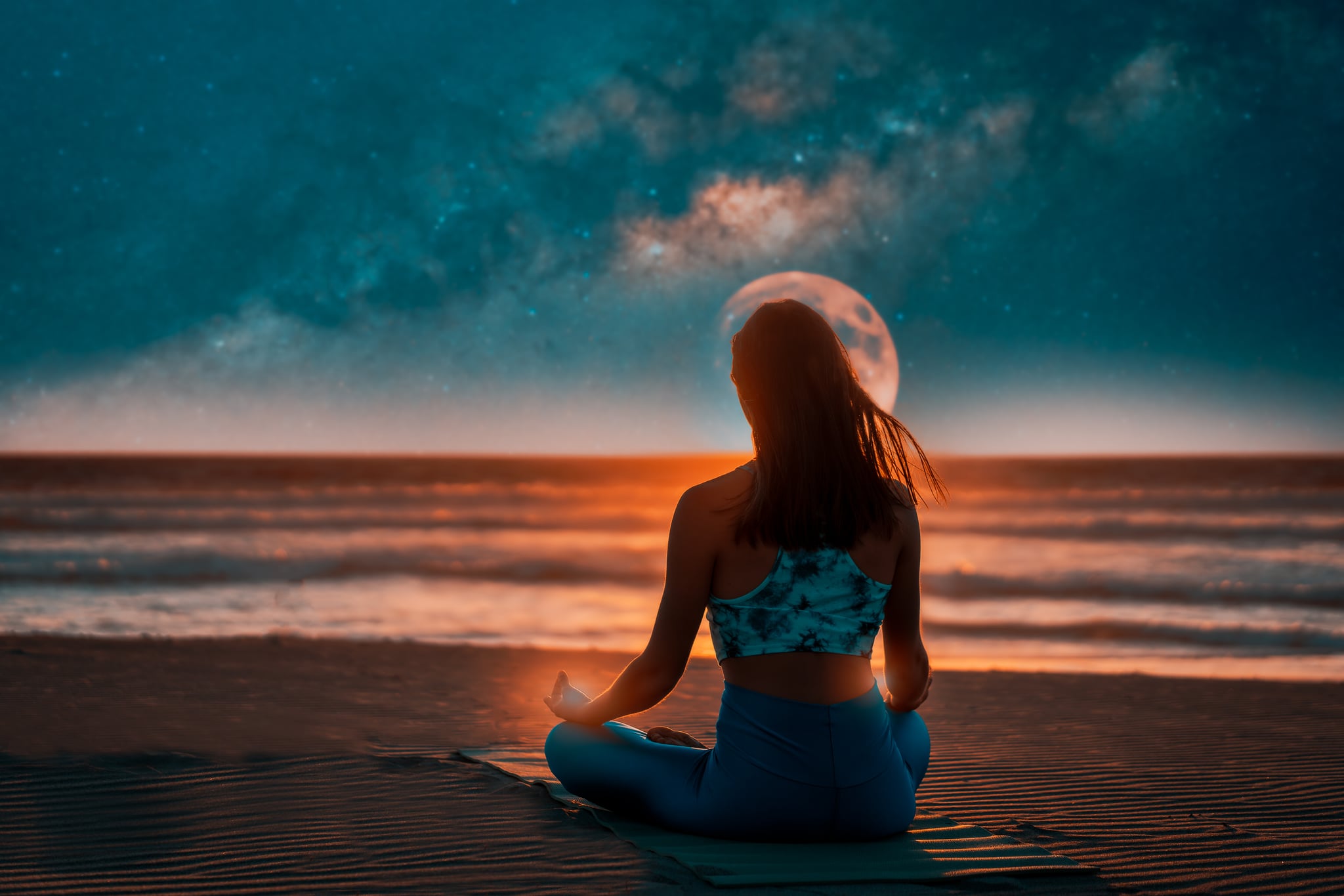 silhouette of a woman on the shore of the beach meditating at night with the moon and milky way in the background over the sea