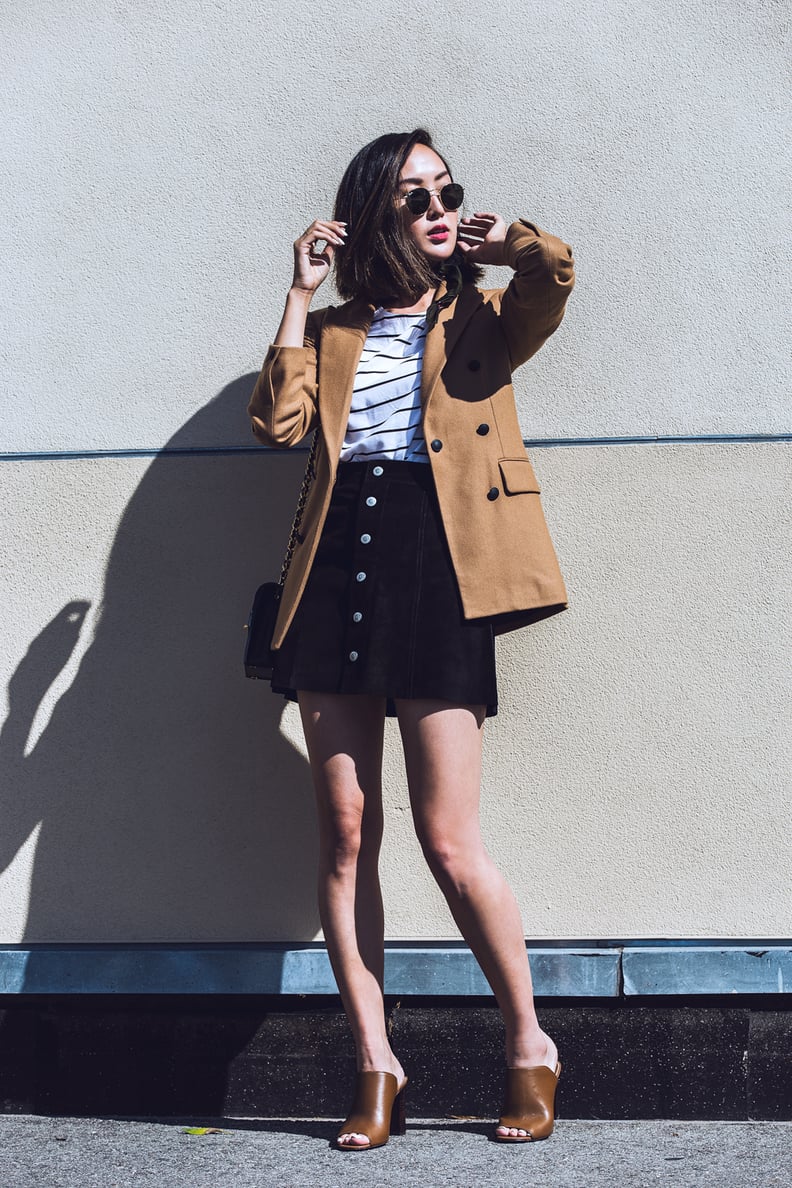 A camel-colored coat over a striped tee, suede skirt, and a pair of mules.