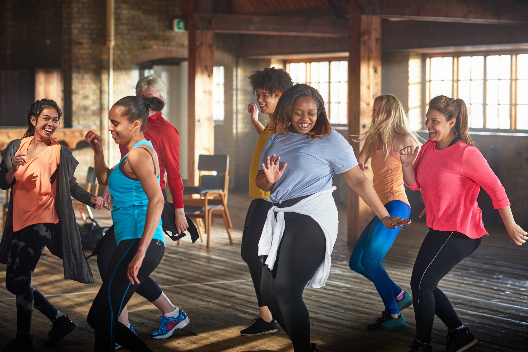 Group of smiling women wearing colorful sports clothing dancing in gym.