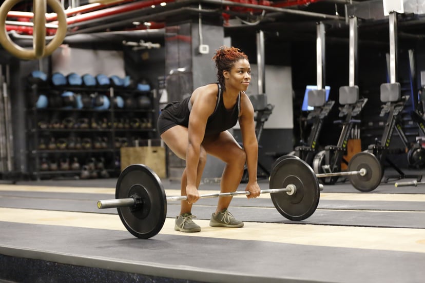 Fit, young African American woman working out with barbells in a fitness gym.
