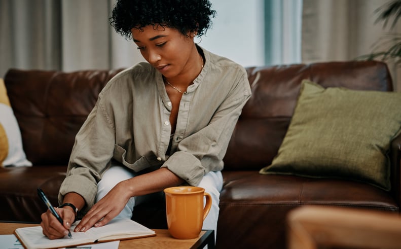 Woman writing daily affirmations in a notebook while sitting on her couch.