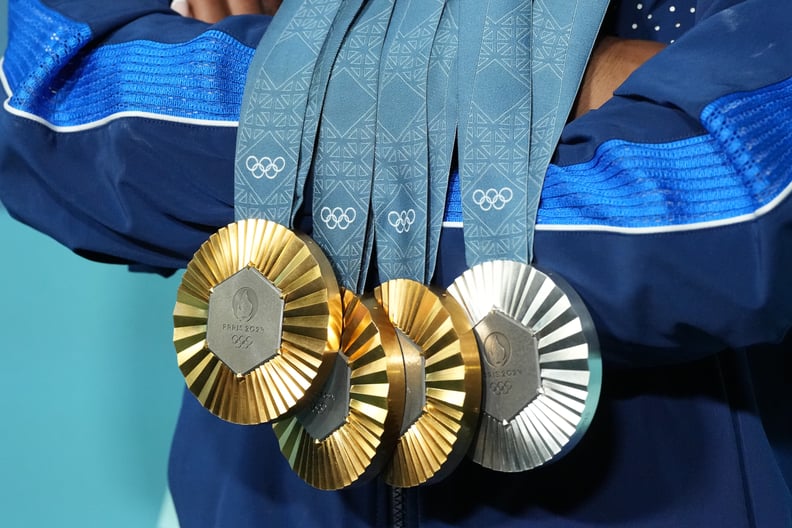 a close up of Team USA Simone Biles posing victorious with her three gold and one silver medal