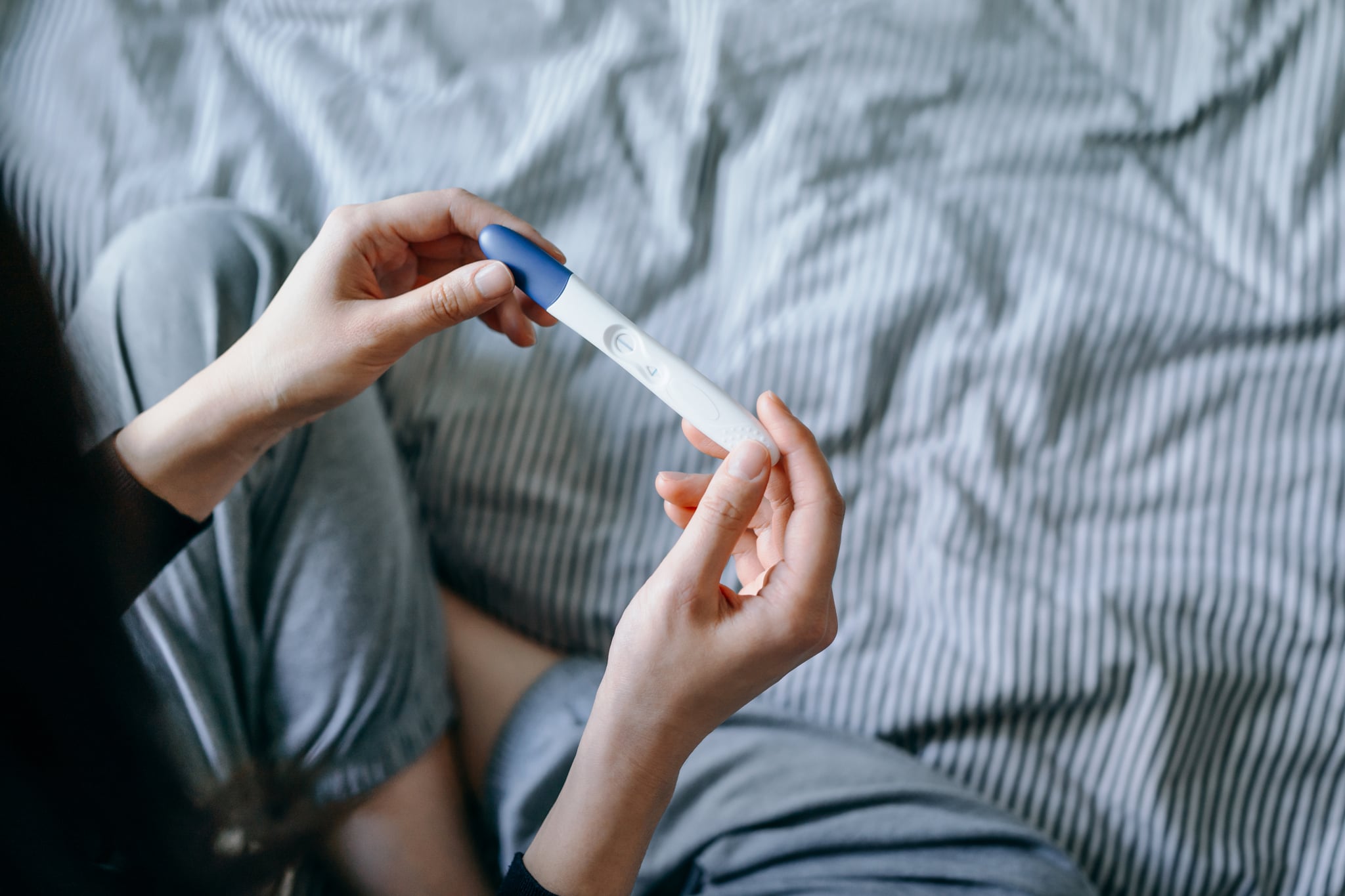 High angle view of disappointed young woman sitting on the bed and holding a negative pregnancy test. 