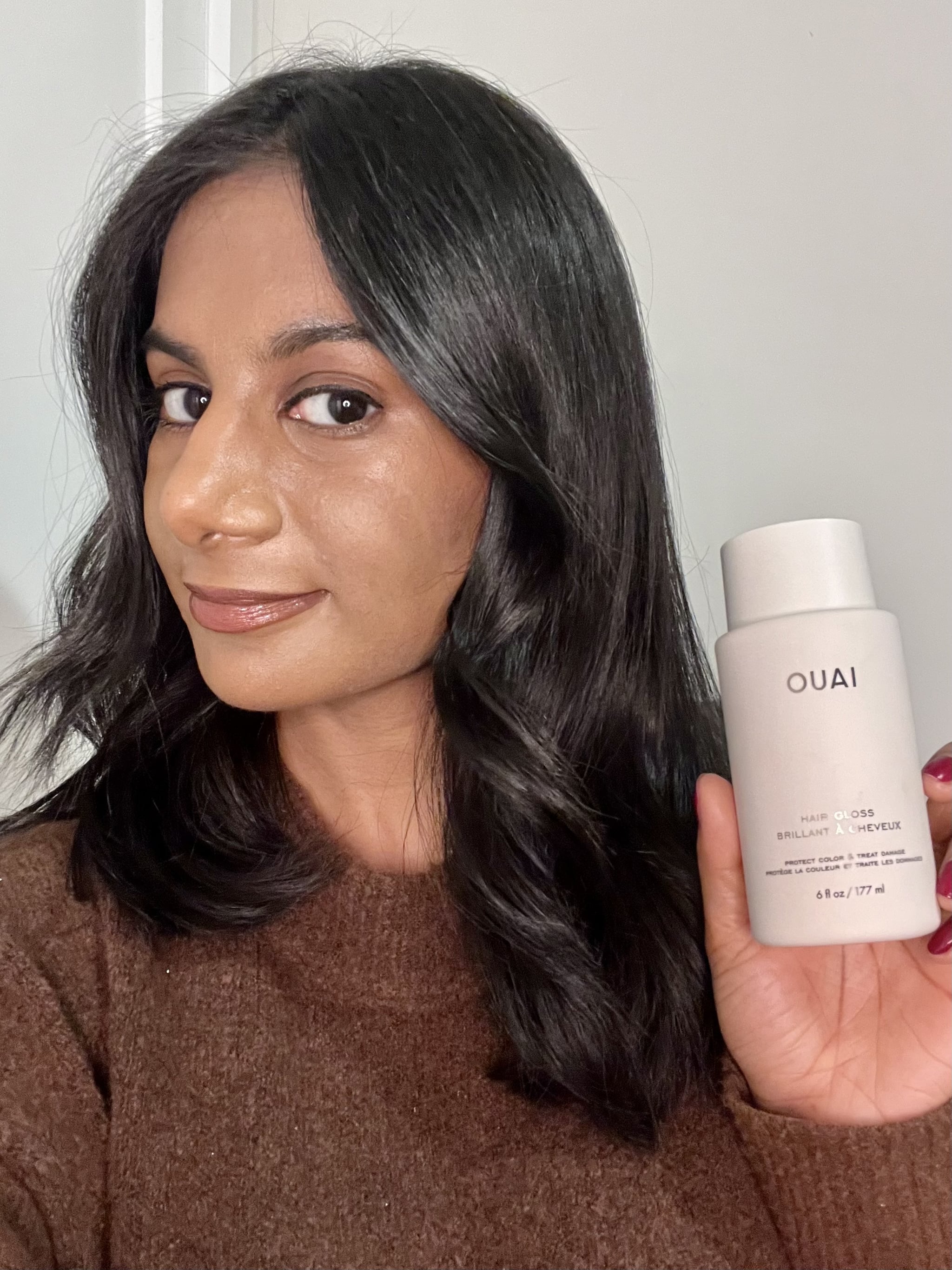 Woman holding the Ouai Hair Gloss and showing the results.