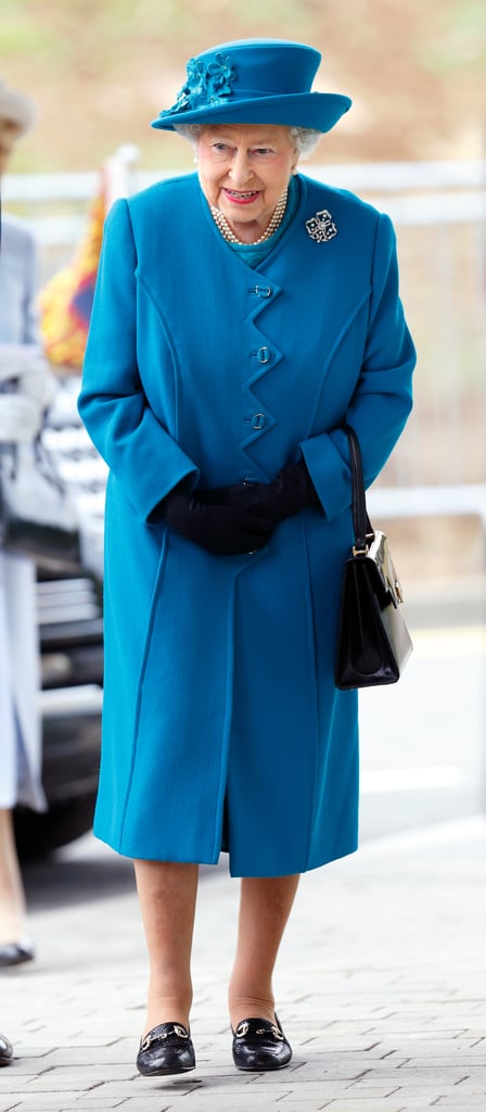 The queen accessorized with black gloves, a square satchel, simple loafers, and the perfect top hat, designed by Rachel Trevor-Morgan and embroidered with a bouquet of blue flowers.