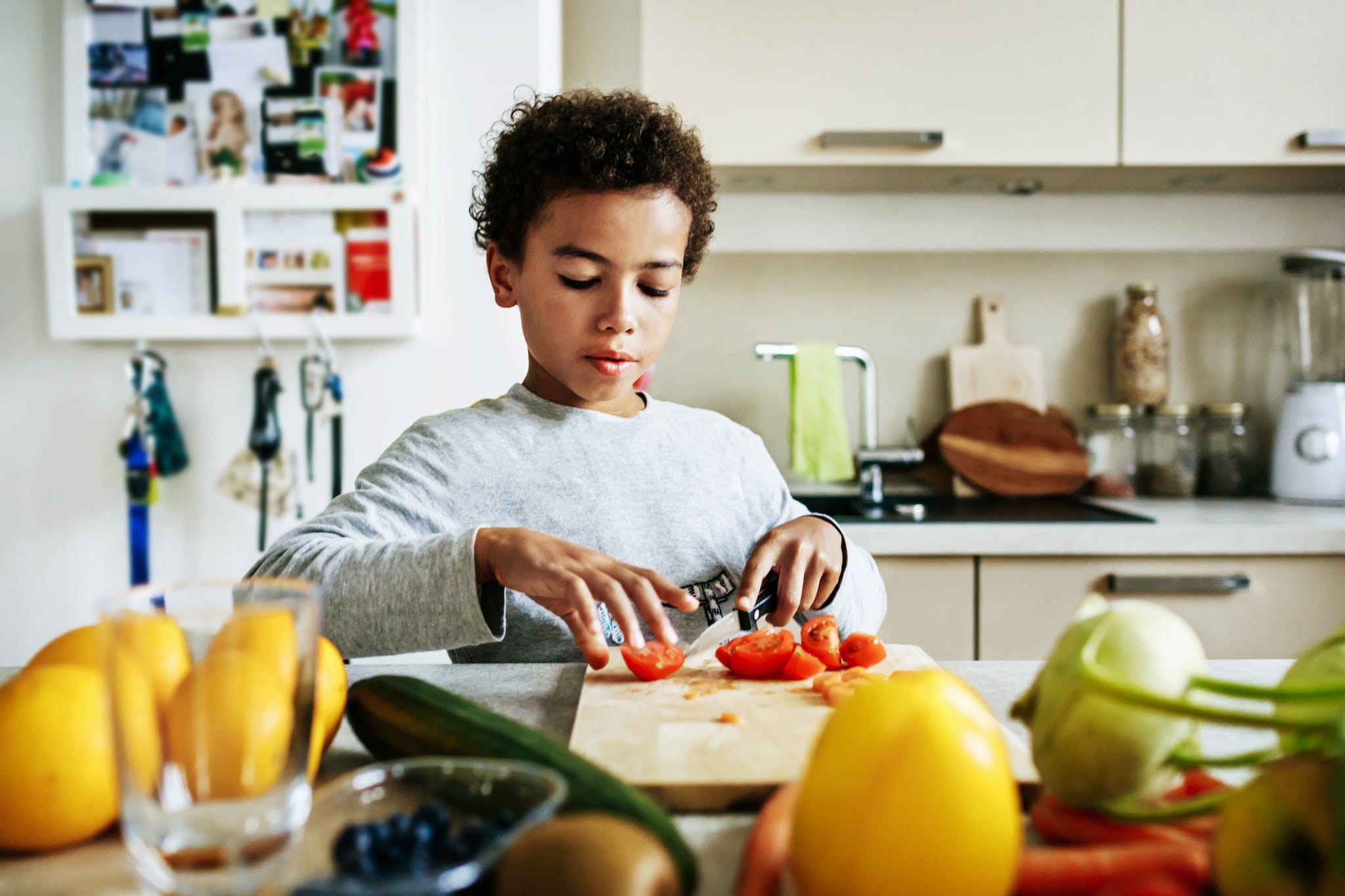 A young boy at home helping his dad to prepare lunch by slicing some tomatoes.