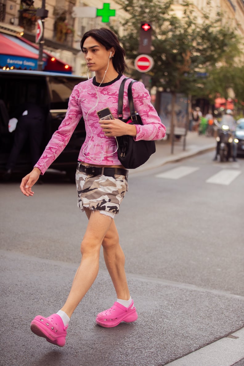 PARIS, FRANCE - JUNE 24: A guest wears a pink longsleeve peplum knit camouflage top, low-rise gray camouflage caro mini skirt with a black belt, hot pink Crocs, and white socks during Paris Fashion Week Mens Spring/Summer 2023 on June 24, 2022 in Paris, F