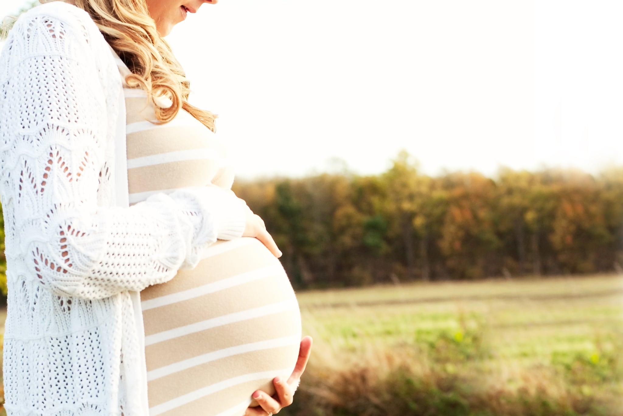 Profile of expectant mother's hands on bump with countryside background.