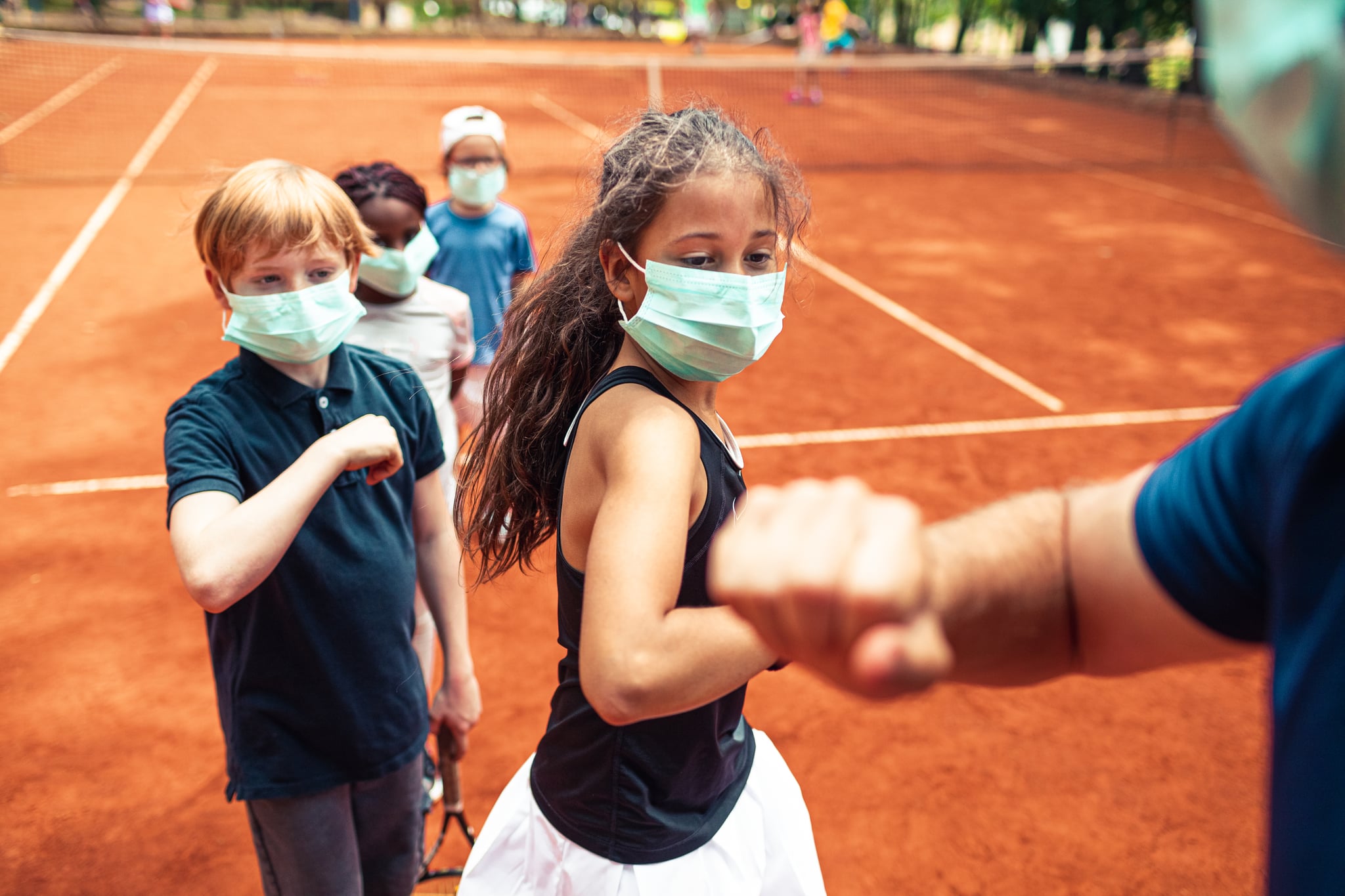 Close up of a group of kids elbow bumping their tennis instructor after practice