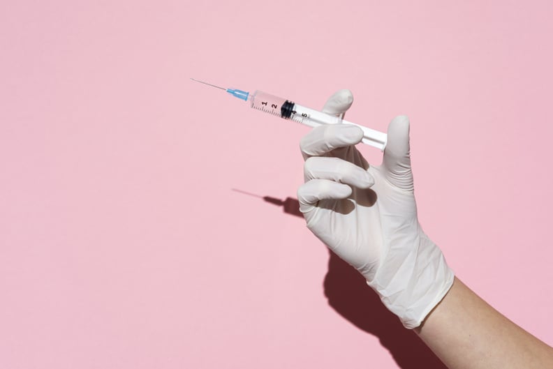 Hand holding syringe in plain pink background.Studio Shot