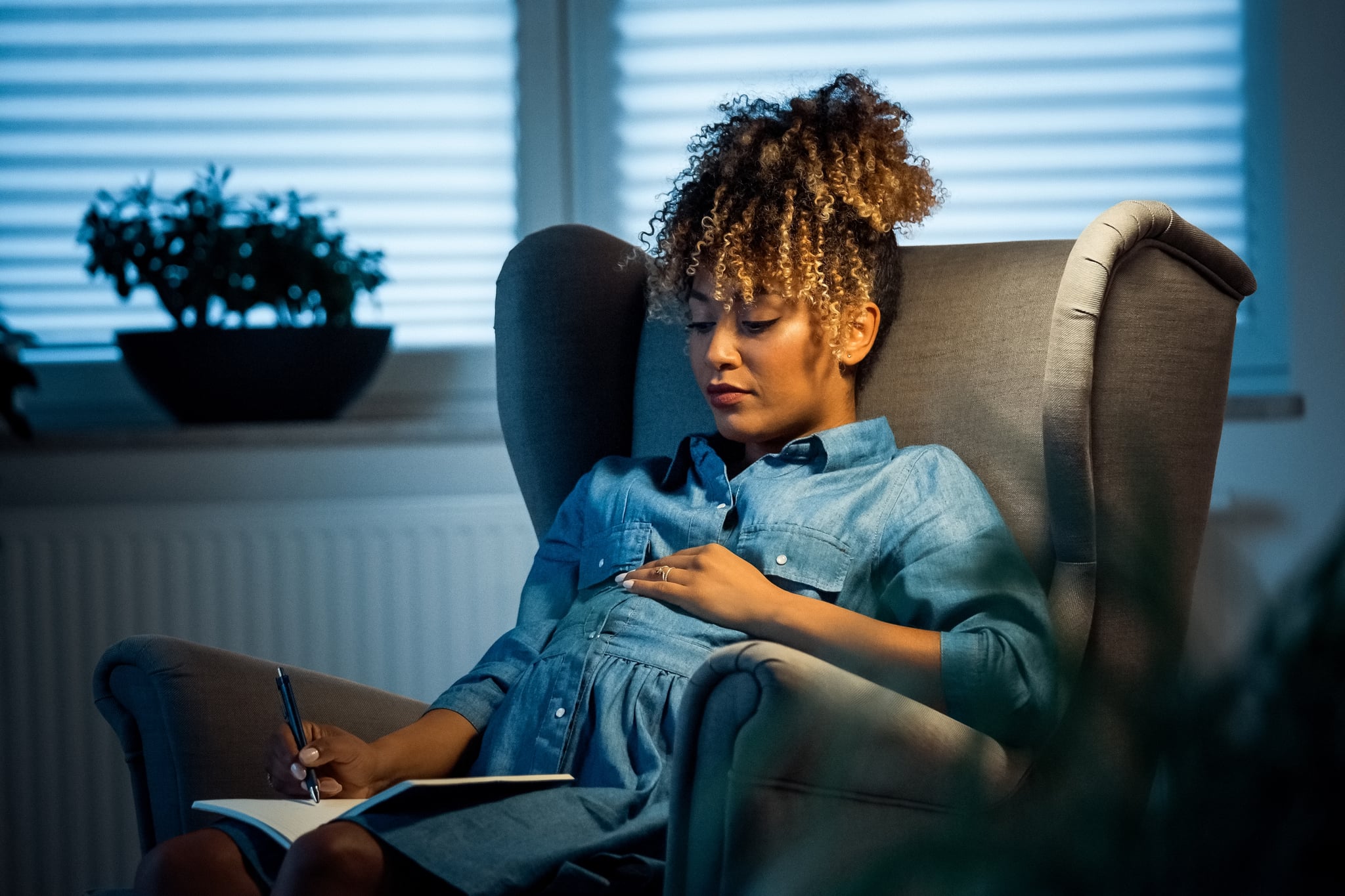 Pregnant expertise resting on armchair in new office. Female professional is wearing business casual. She is writing on book.