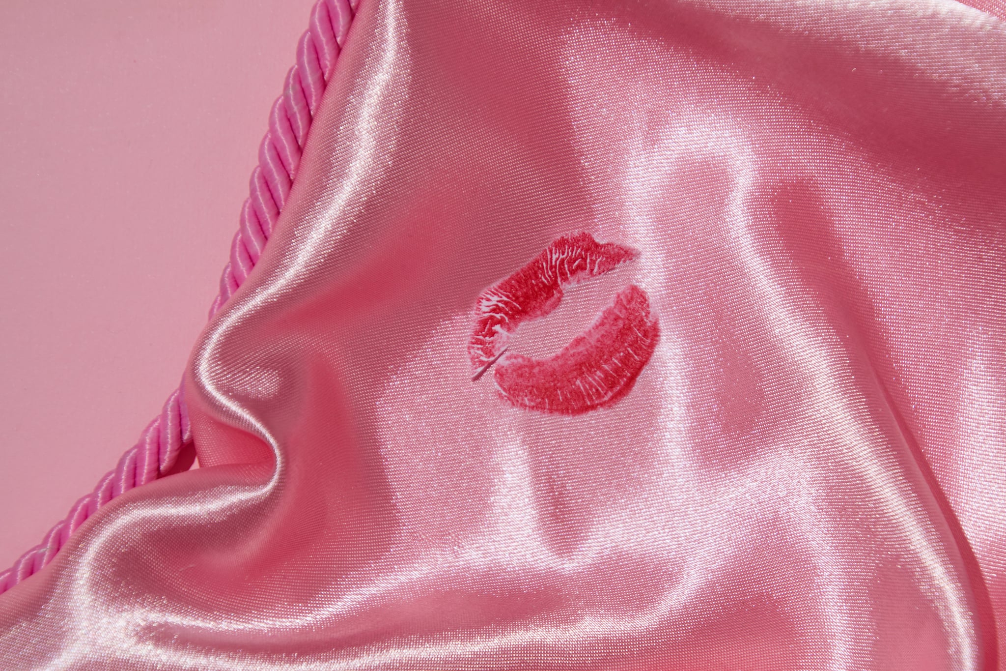 A red lipstick mark on a pink satin sheet