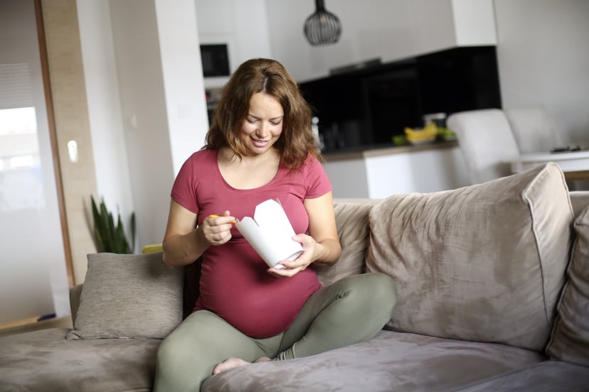 Pregnant woman at home, eating take away food. About 30 years old, Caucasian brunette.