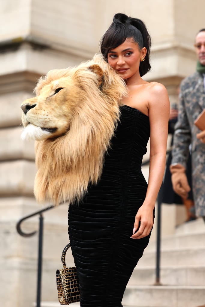 Kylie Jenner is back in couture. On Jan. 23, a day after finally revealing her son's name, the beauty mogul made her grand entrance at Schiaparelli's Paris Haute Couture Week show in quite the striking ensemble: a ruched velvet gown adorned with a giant faux lion's head. While the animal motif certainly stole the show, the rest of the piece wasn't exactly simple — the figure-hugging corset dress came with a lace-up back and a mermaid train. Jenner, who happens to be a Leo, completed the look with black and gold accessories, including gold toe heels, a snakeskin purse, and earrings in the shape of eyes. 
"BEAUTY AND THE BEAST. thank you @danielroseberry and @schiaparelli for such a special morning. wow i loved wearing this faux art creation constructed by hand using manmade materials. beautiful beautiful," she wrote alongside photos from the show. Jenner wore the creation sitting front row, as a similar version debuted on the runway. Modeled by Irina Shayk, the catwalk version featured a long, one-shoulder silhouette and straight skirt. 
The always-extravagant Schiaparelli couture collection included other designs based on lifelike creatures like a snow leopard, snake, and wolf, in addition to horned bustiers and dramatic embellishments. Fellow front row attendee Doja Cat also wore a shocking look, arriving at the show covered in head-to-toe red body paint and 30,000 Swarovski crystals.
Following a series of casual looks from Jenner, like a cutout onesie from Skims and matching Jean Paul Gaultier sets with best friend Stassie, the beauty brand founder has upped the ante for Paris Couture Week. See more photos of her show-stopping outfit ahead, then see what she wore to the Maison Margiela presentation. 

    Related:

            
            
                                    
                            

            Kylie Jenner&apos;s Fishnet Catsuit Is Sheer From Head to Toe