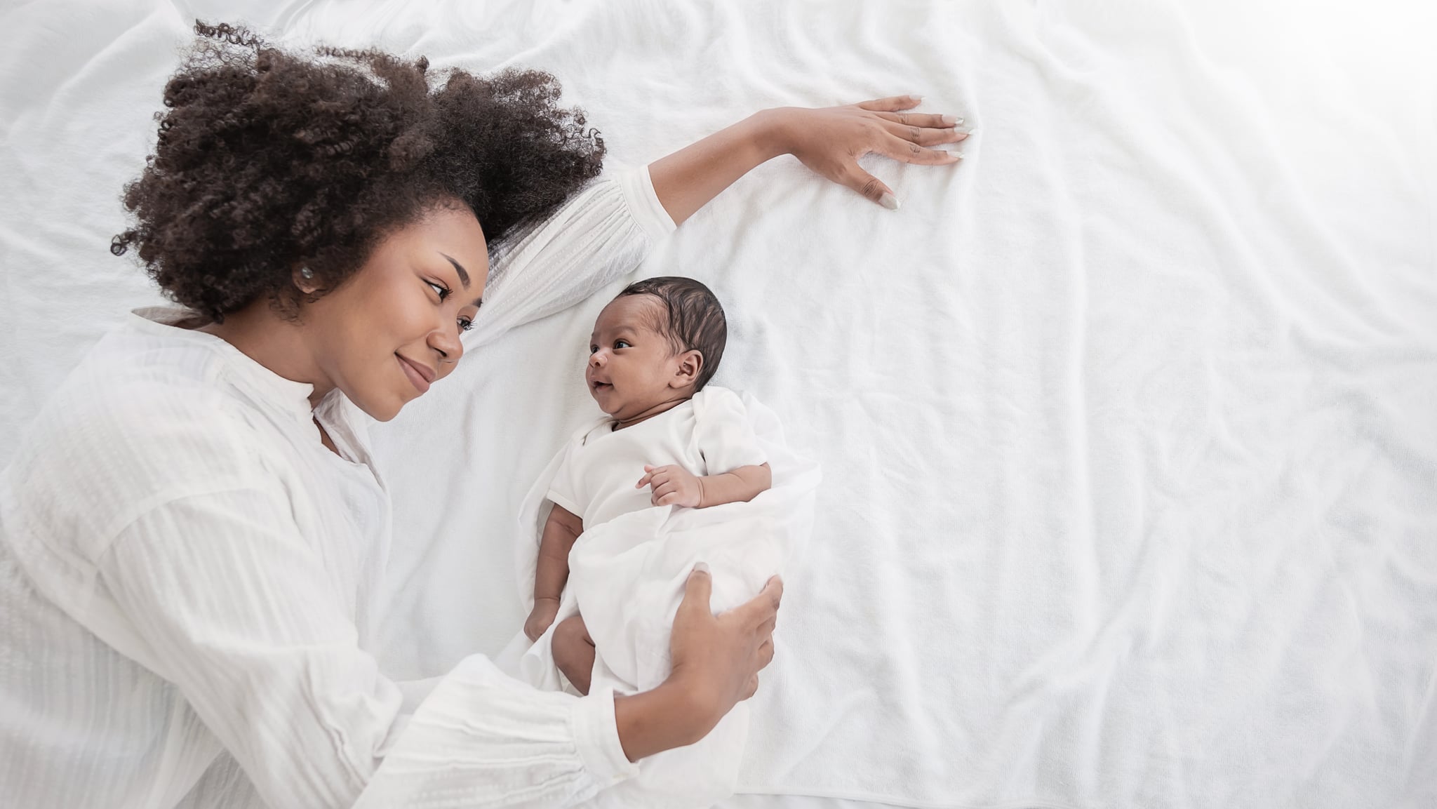 特写肖像美丽年轻的非洲裔美国人的母亲一天女孩吻健康新生儿睡在床上平复制空间。医疗保健医疗爱黑人女性生活方式的母亲节,俯视图