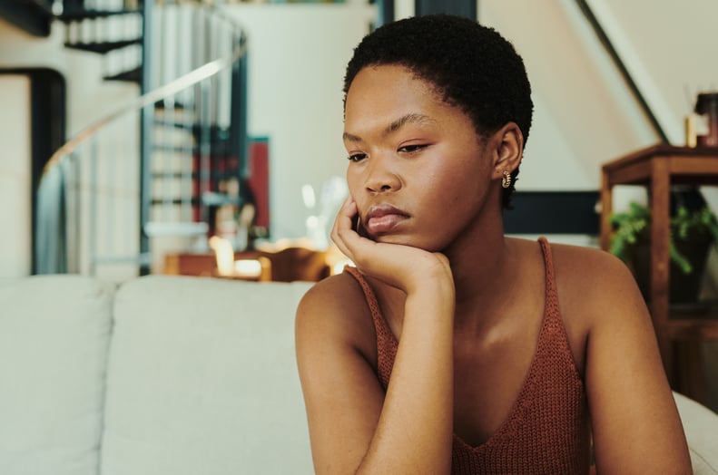 young woman on her couch thinking whilst sitting with her hand under chin