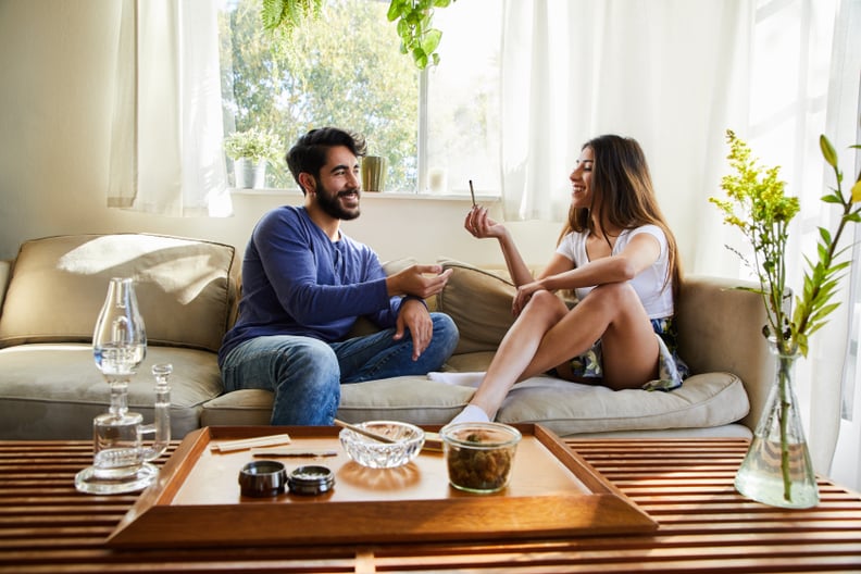 Young couple smoking a joint together while sitting on their living room sofa at home discussing stoner date ideas.