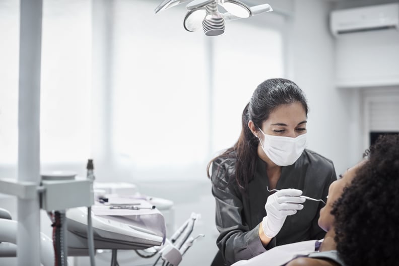 Female dentist examining teeth of patient on chair. Young woman is visiting doctor for dental checkup. They are at clinic.