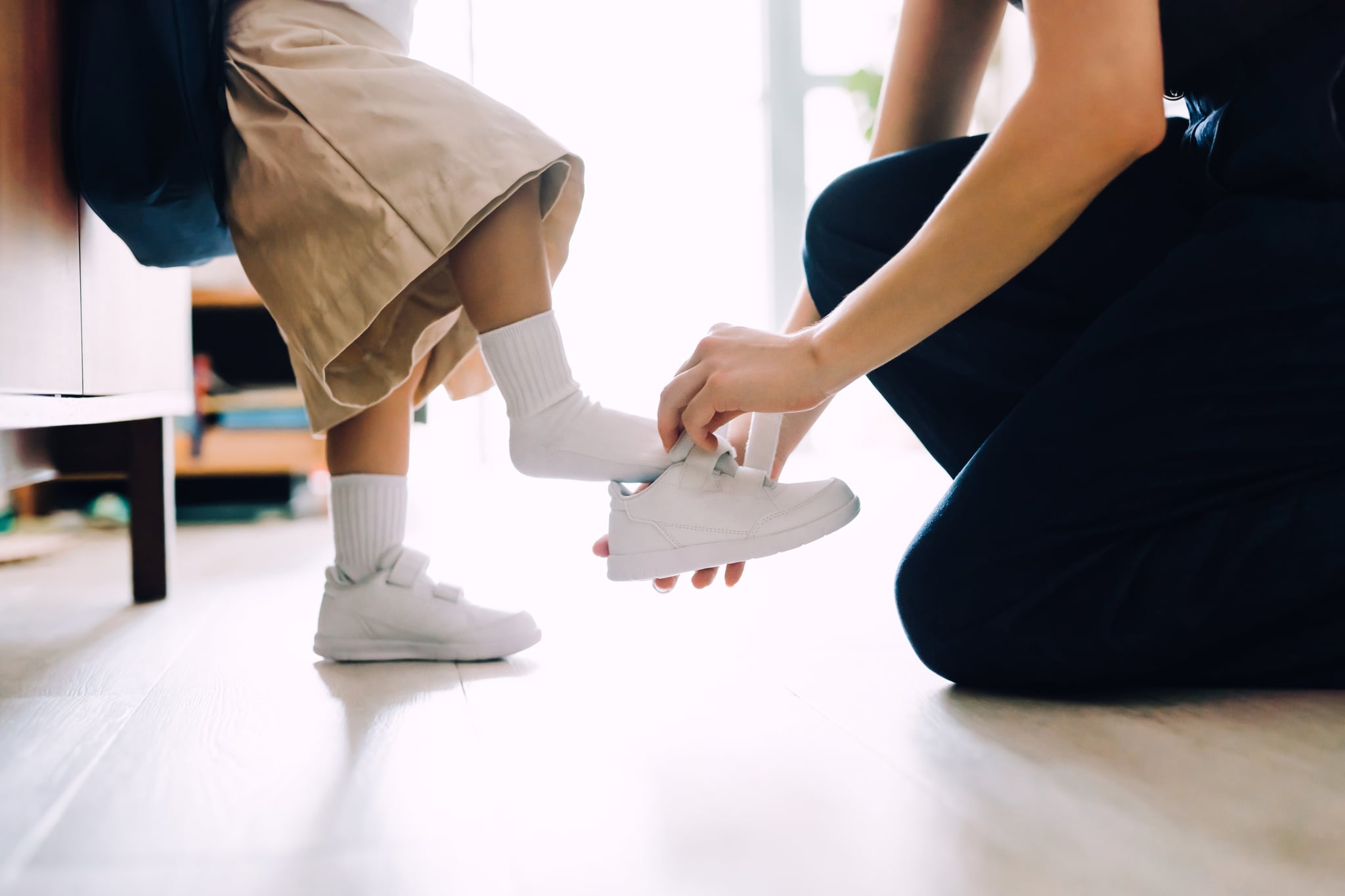 Close up of young Asian mother putting on shoes for her little daughter in the living room and preparing for her first day at school