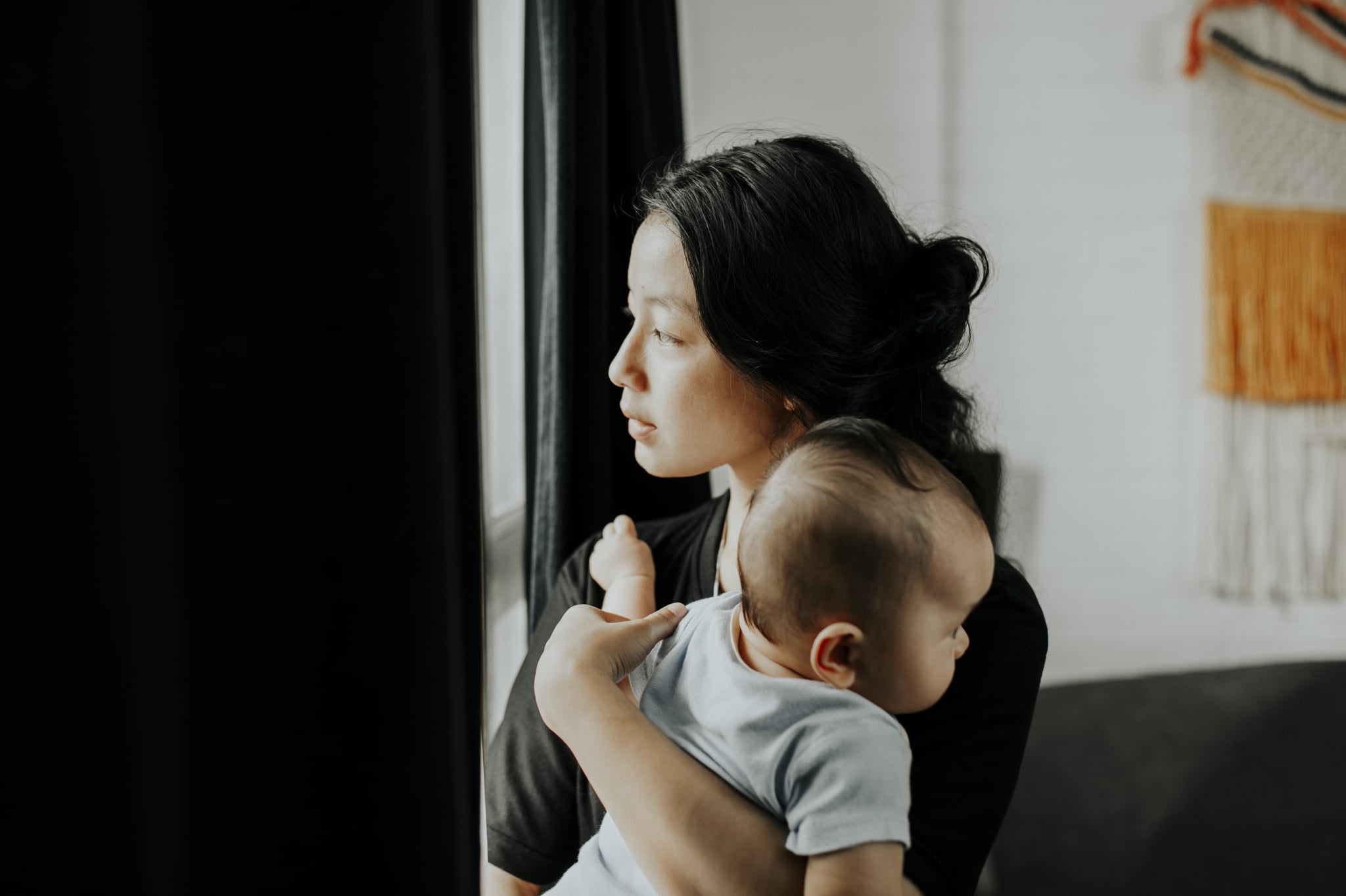 Young woman carrying baby looking throughout window.