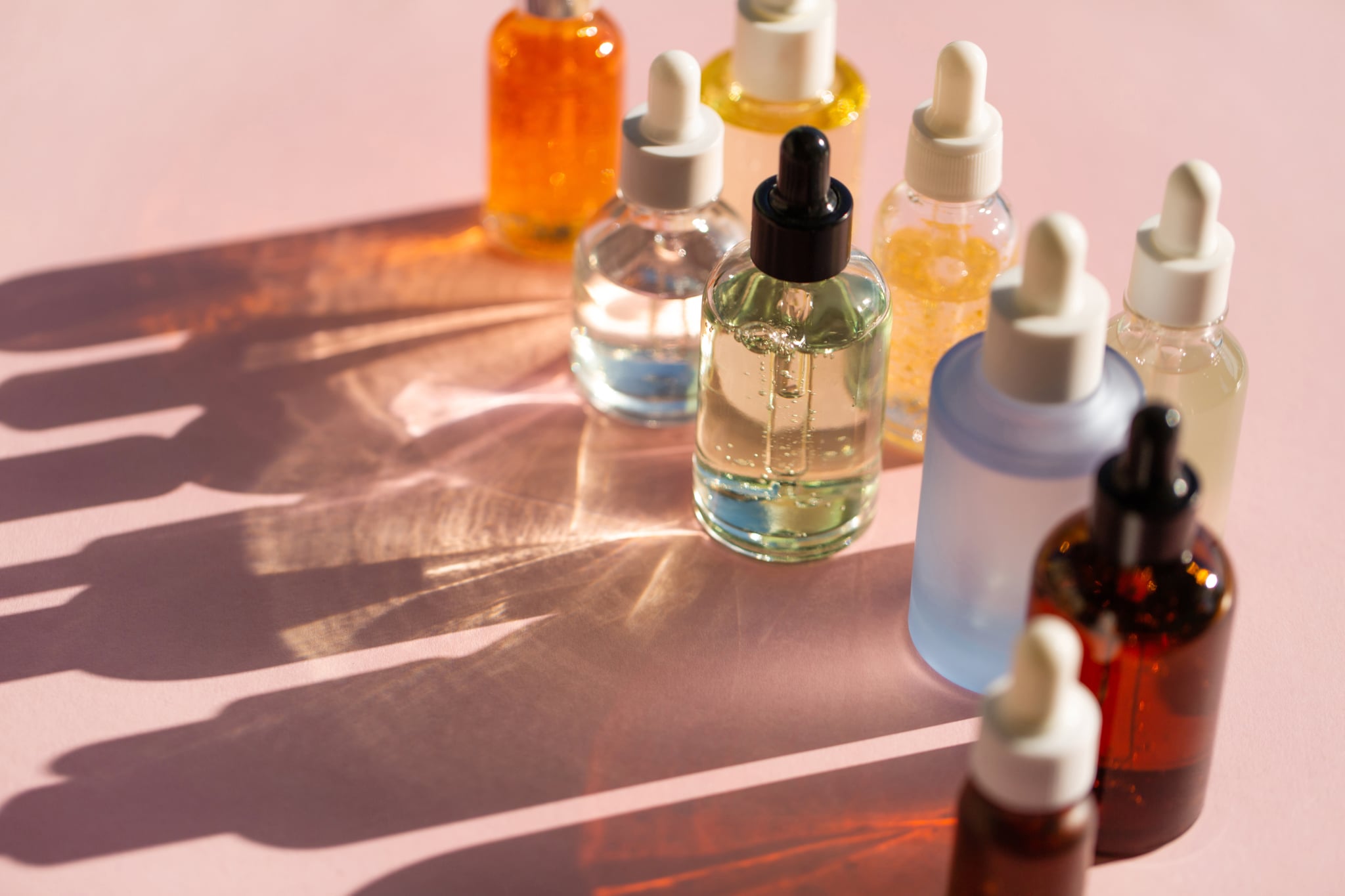 Top view of set of bottles with assorted organic essential oils and natural lotions casting shadow on pink background. Good for your design. Serum is the most popular beauty product of the year