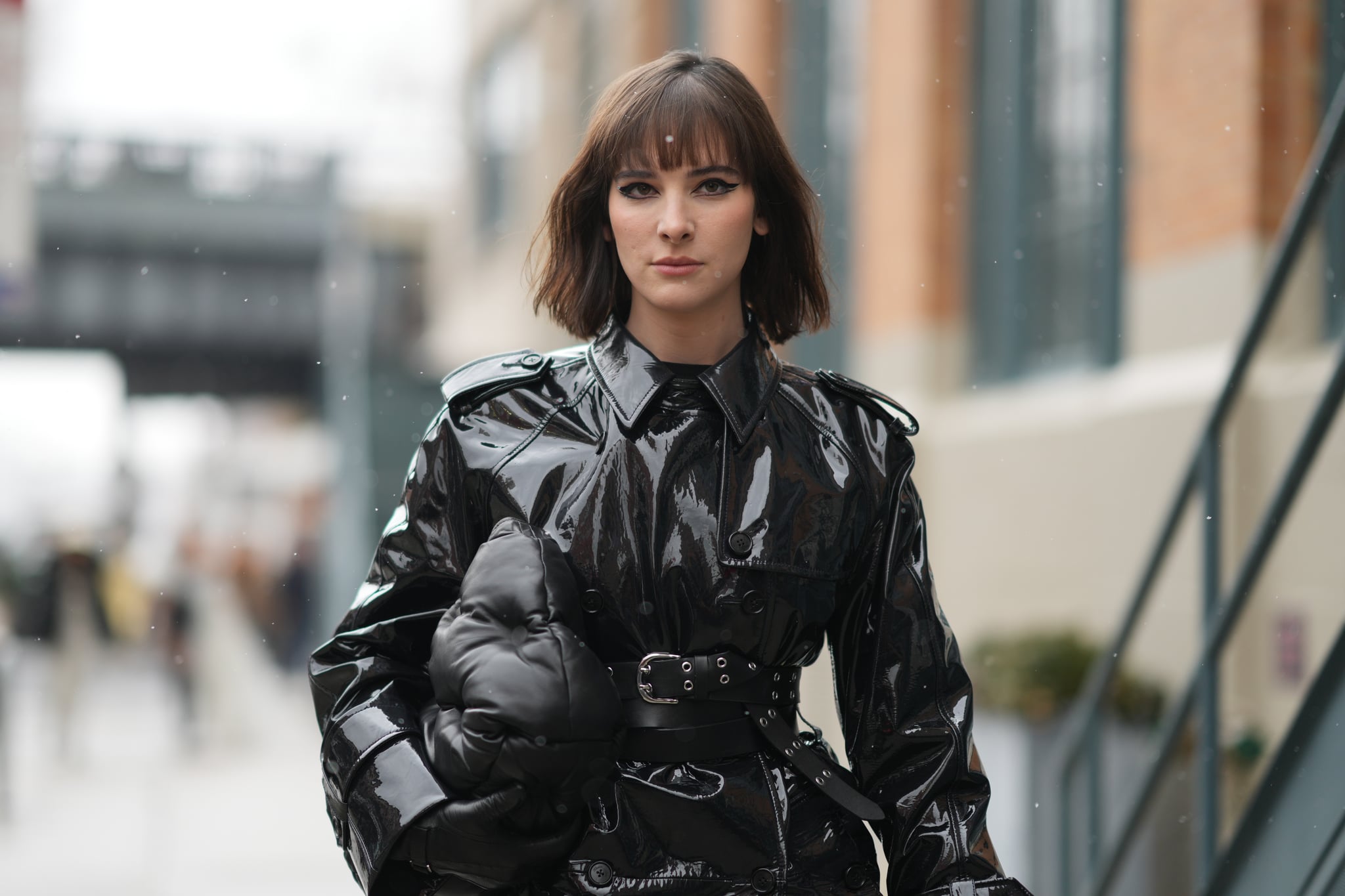  Hari Nef wears a black high neck pullover, a black shiny vinyl belted long trench coat, a black matte puffy leather handbag from Bottega Veneta, a black shiny leather nailed / studded belt, outside Khaite, during New York Fashion Week, on February 13, 2022 in New York City. (Photo by Edward Berthelot/Getty Images)