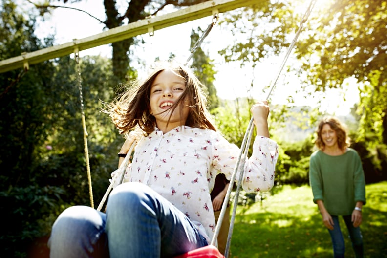 Cheerful mother pushing daughter on swing in sunny park