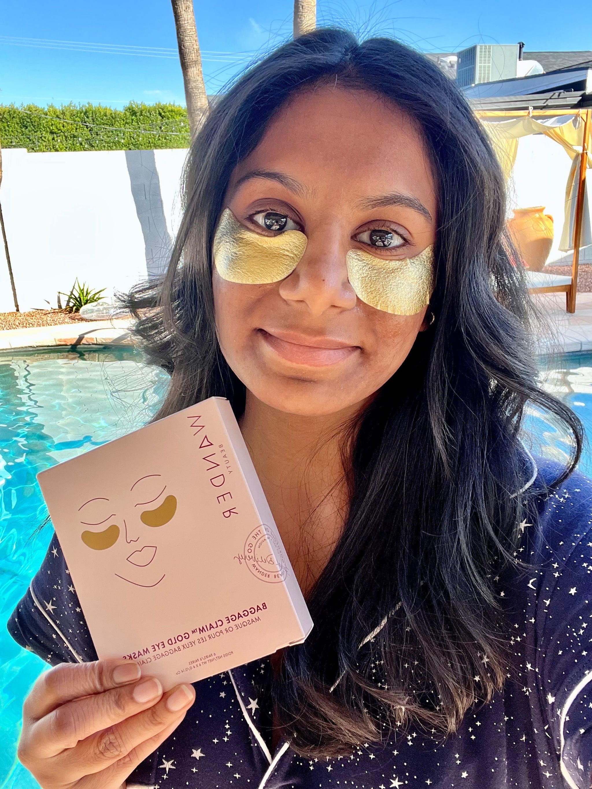 Woman wearing the Wander Beauty Baggage Claim Eye Masks and holding the product.
