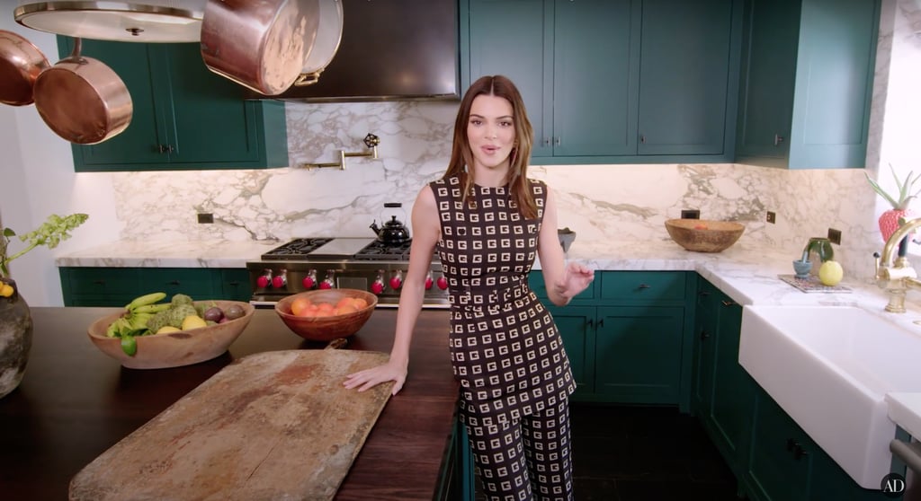 The cabinets are painted a deep teal colour, and copper pots hang above the centre island.