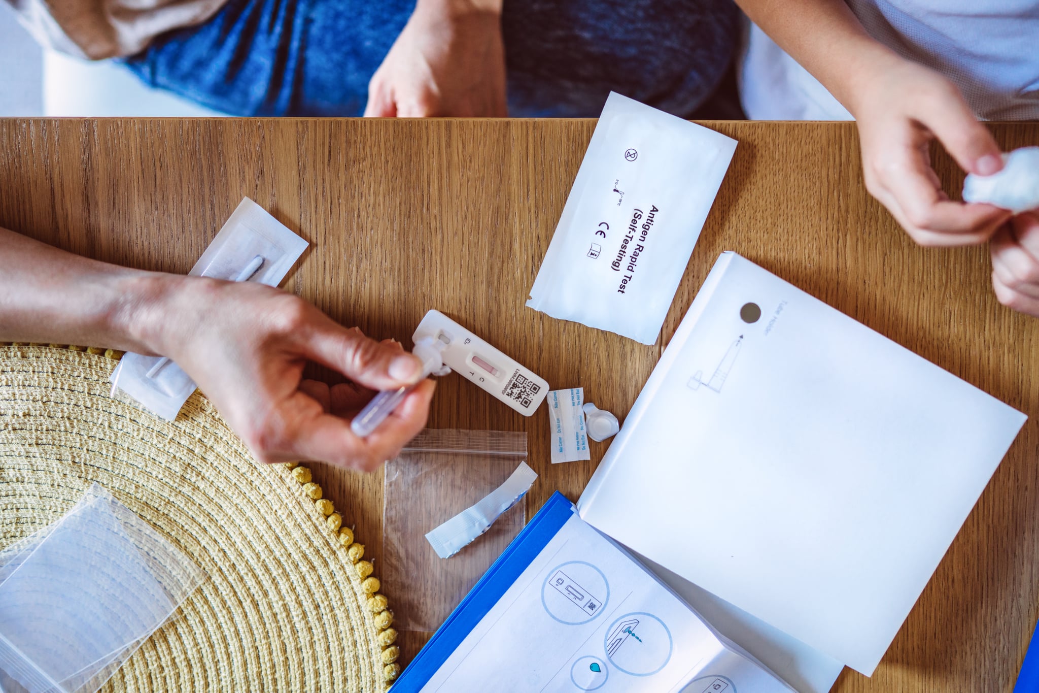 Directly above view of mom squeezing the sample liquid on a test strip while carrying out a Covid-19 rapid self test for her kid at home.