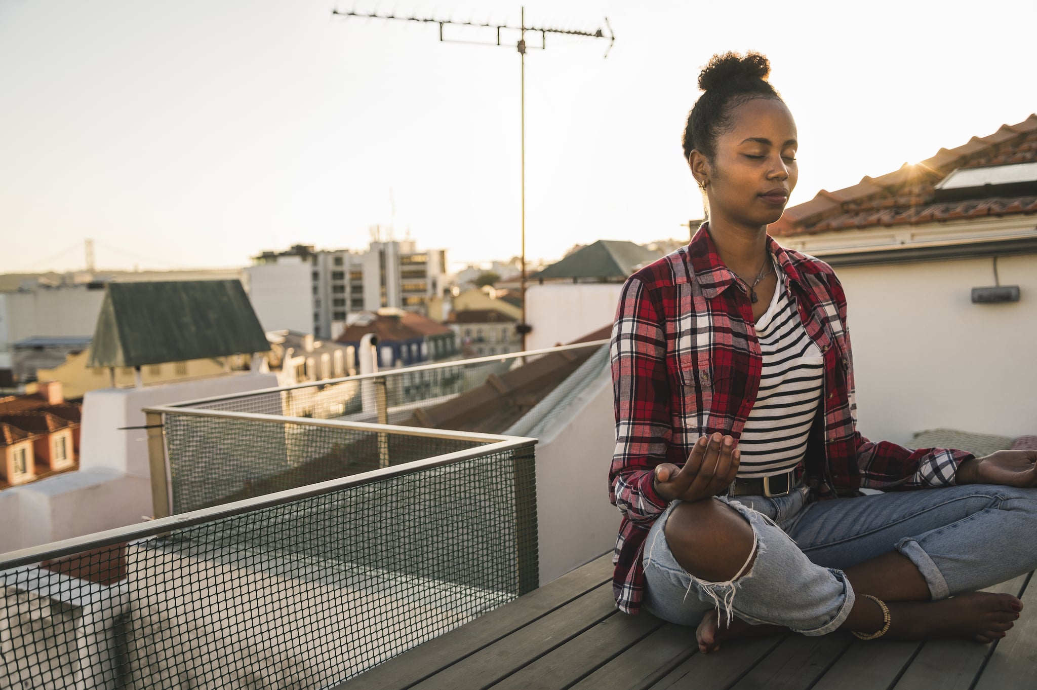 Young woman practicing yoga on rooftop at sunset