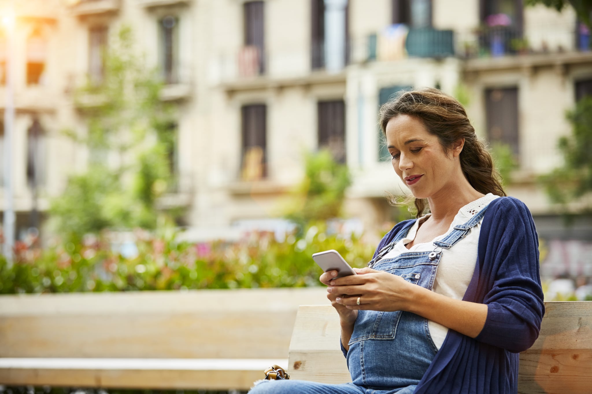 Pregnant woman text messageing while sitting on bench