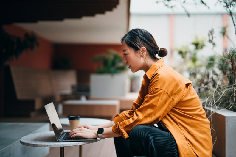 Woman working alone on her laptop at an outdoor cafe in an orange shirt.