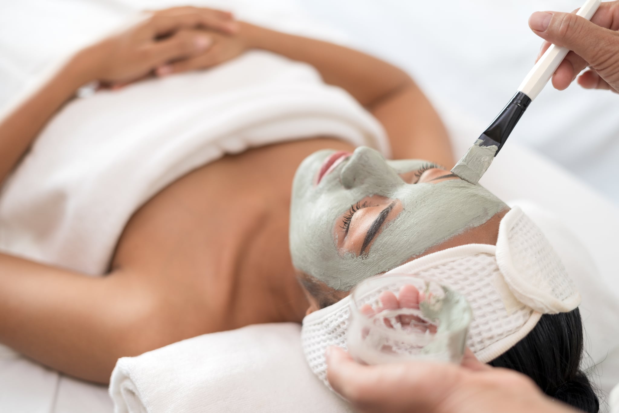 Close up of beautician applying clay mask on woman's face during beauty treatment in spa