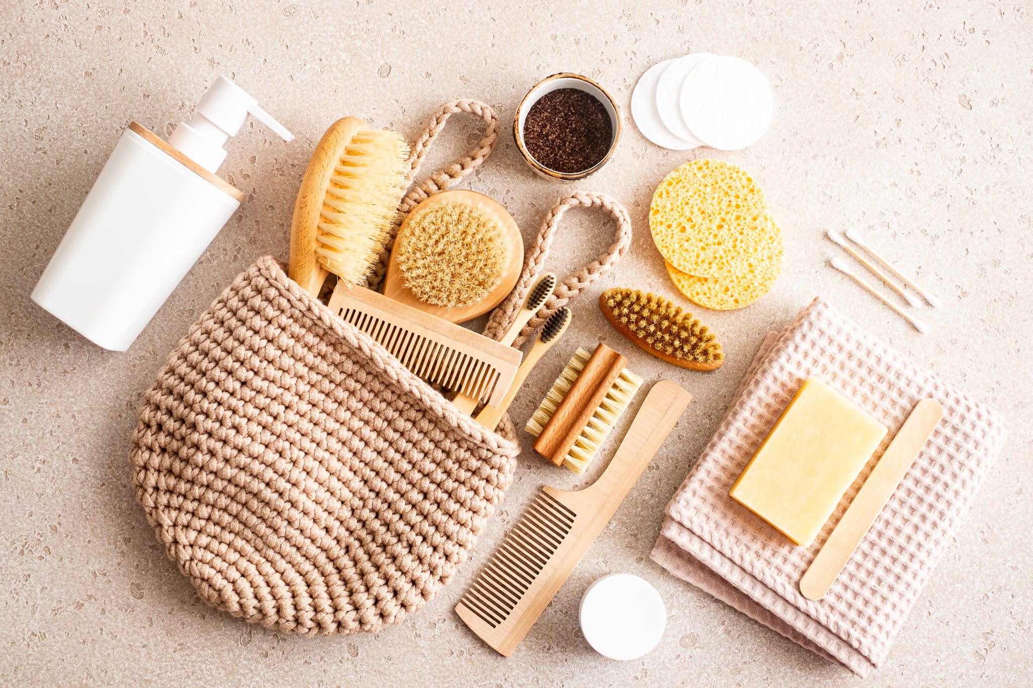 Close-up of wooden dry skin body brushes, bamboo tooth brushes, hair brushes, nail brush, cotton swabs and pads, cup of coffee scrub and soap dispenser on concrete background, top view. Spa at home, flat lay. Zero waste concept. Eco friendly self-care kit