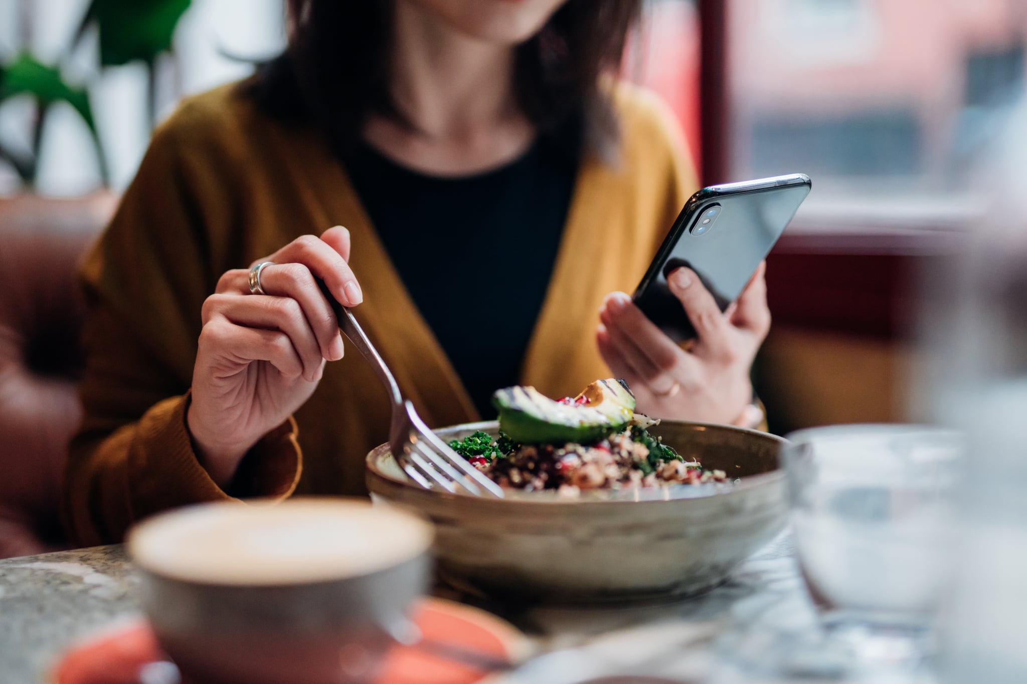 Young woman checking social media on smart phone while eating avocado and quinoa salad.