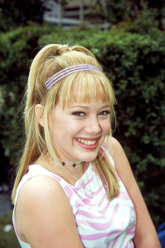 Wearing a pink zebra-print top with multiple necklaces and a pink headband.