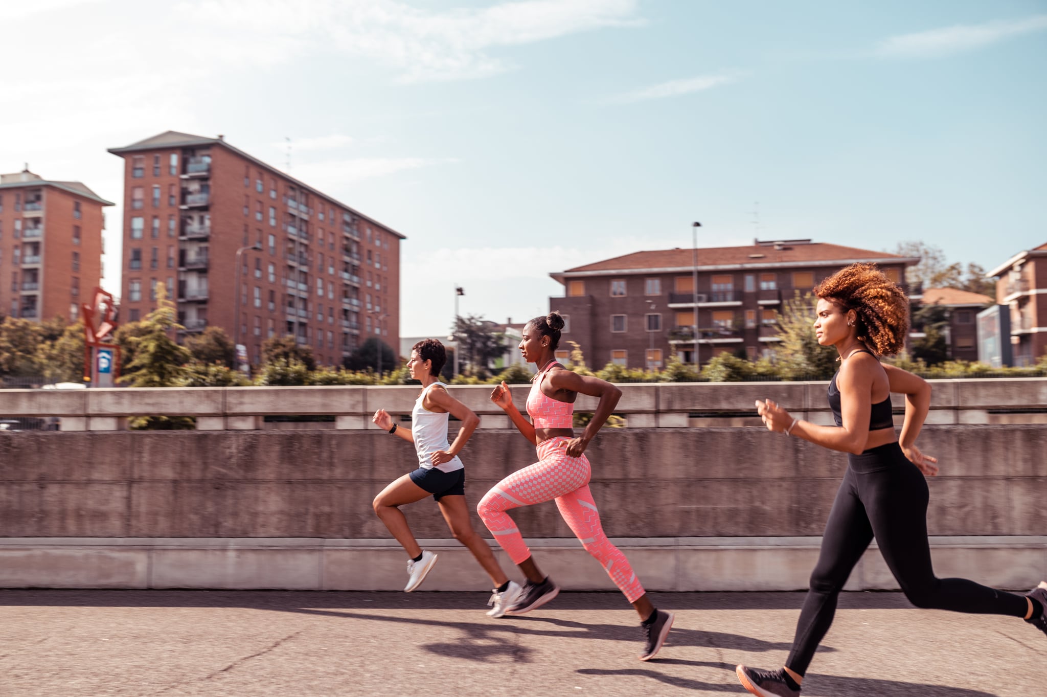 Side view of a three young athletes running on a concrete path in the city