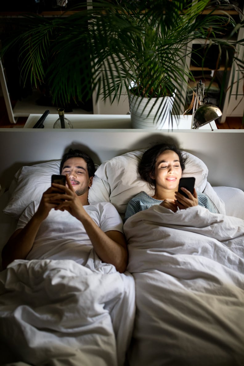 Happy young couple lying together in bed at home and using their mobile phones