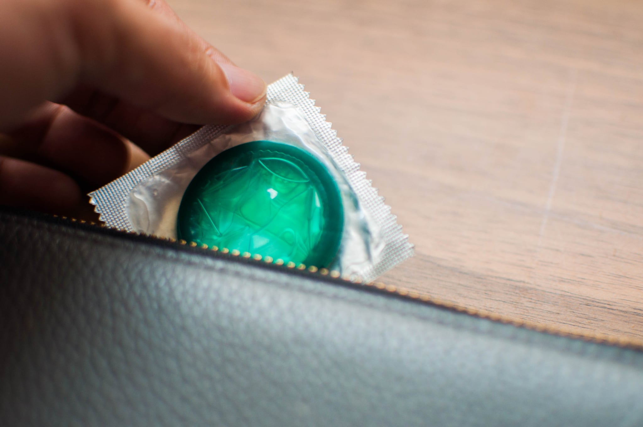 Close up of young man's hand holding a condom from wallet on the table