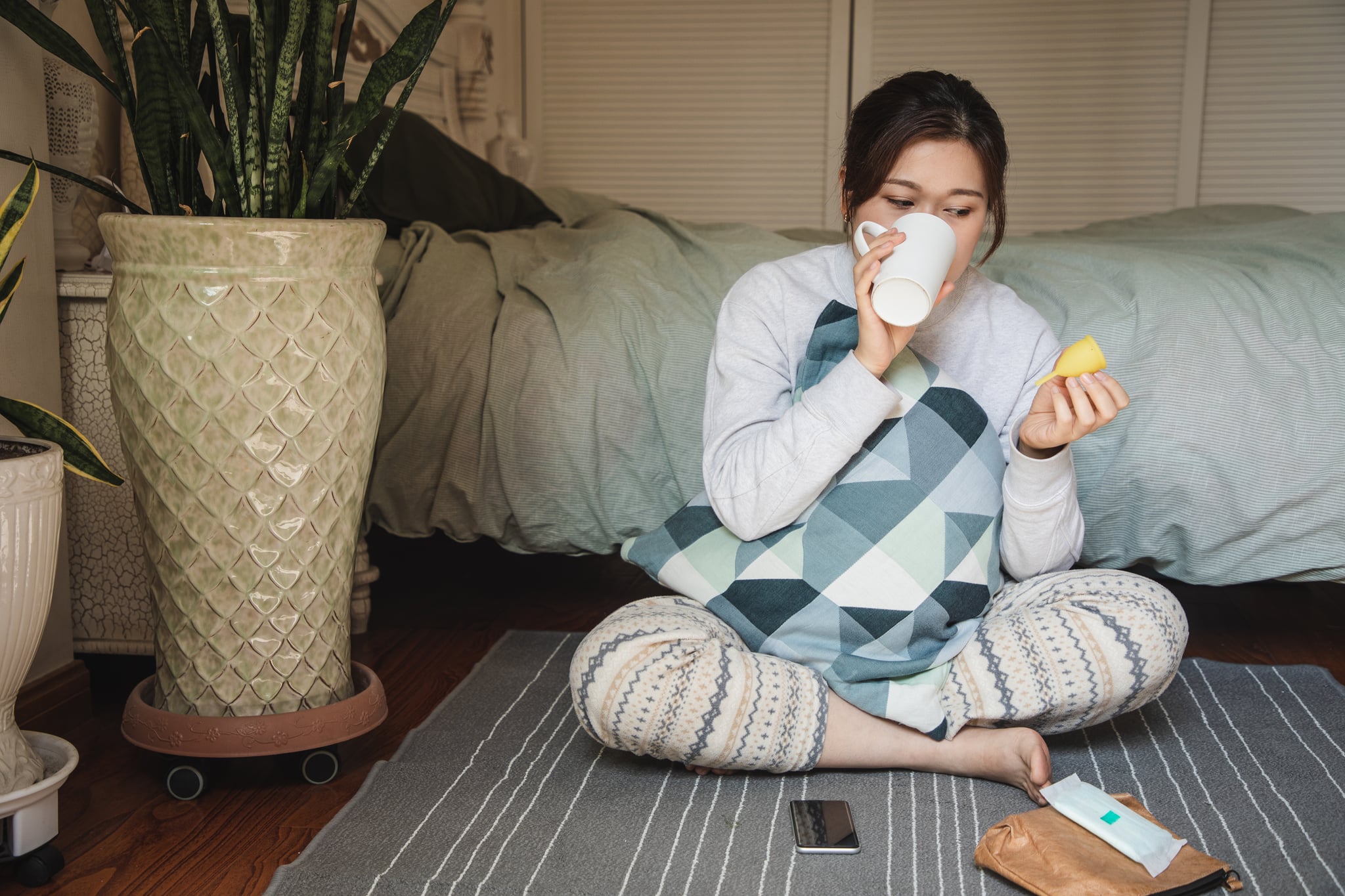 亚洲女人拿着月经杯,饮用水在她的卧室