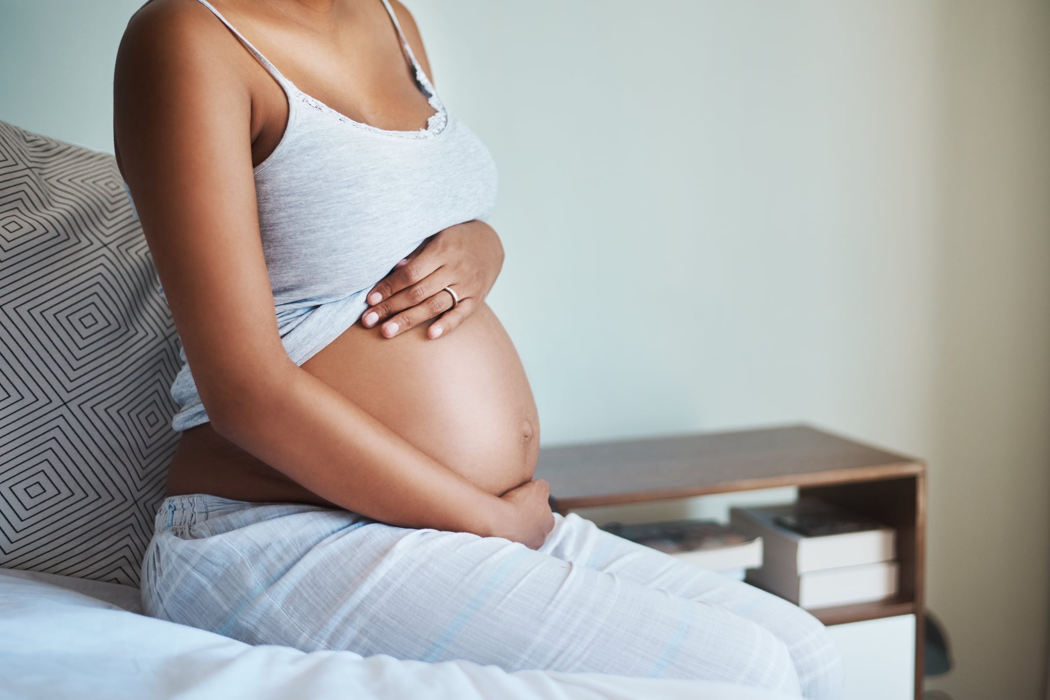 Shot of an unrecognizable pregnant woman sitting on a bed and holding her belly in her bedroom at home