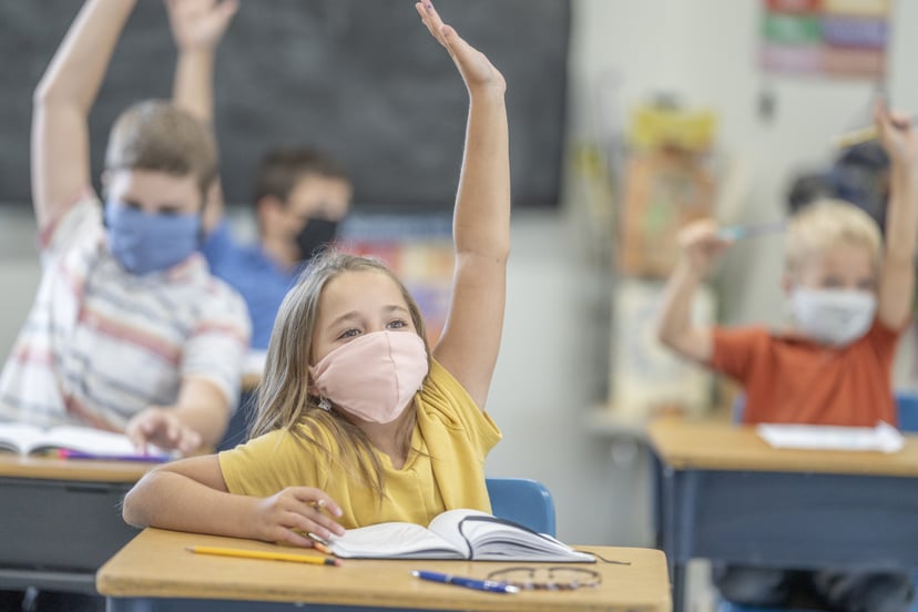 Group of students wearing protective face masks while raising their hands in class.