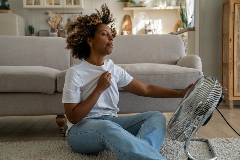 Young woman cooling down by sitting on the floor in front of a fan at home.