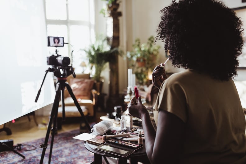 A photo shows a Black beauty content creator making a video with lip gloss.