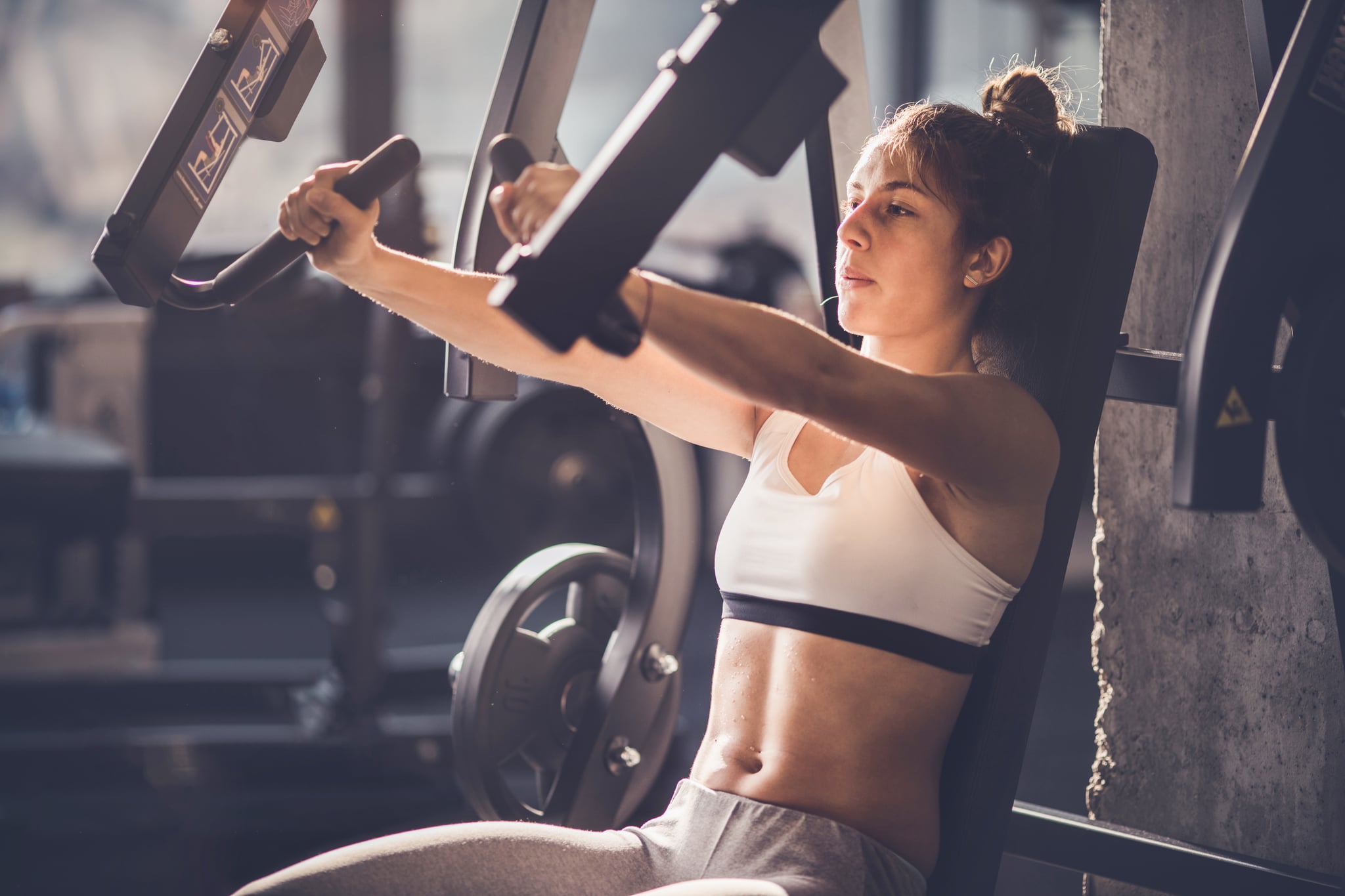 Young athletic woman doing strength exercises on a machine in a health club.