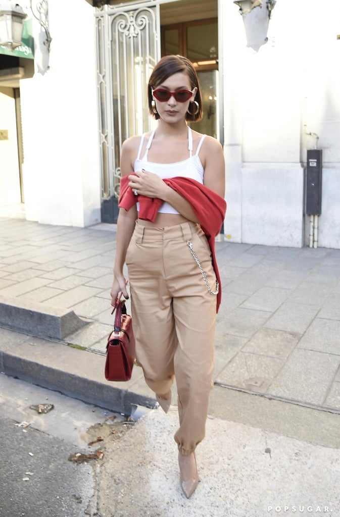 Bella Wore a White Crop Top, Beige High-Waist Trousers, and a Red Sweater Hanging Around Her Shoulders