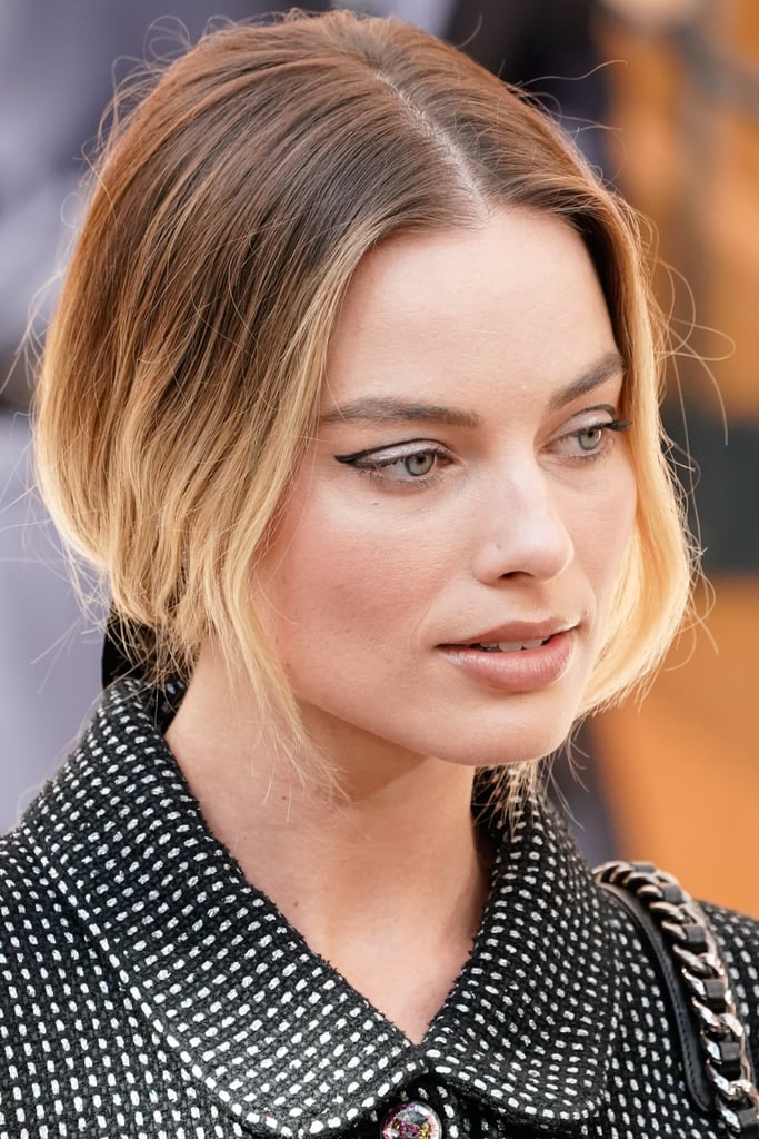 Margot Robbie is taking inspiration from one icon these days. Ahead of the release of Once Upon a Time in Hollywood on July 26, the actress has continued to pay tribute to Sharon Tate, whom she portrays in the '60s-set film. The latest example comes from the Chanel show during Paris Haute Couture Fashion Week, which Robbie attended wearing negative-space eyeliner reminiscent of the "floating" eye makeup Tate actually helped popularize, along with other It girls like Edie Sedgwick and Twiggy. 
Robbie's retro makeup was done by her go-to artist Pati Dubroff, who balanced out the graphic cat eye with nude lipstick and subtle rosy cheeks. Though she's a beauty trendsetter in her own right, it's touching to see Robbie pay homage to the late actress. See photos of the look ahead, as well as the original inspiration.