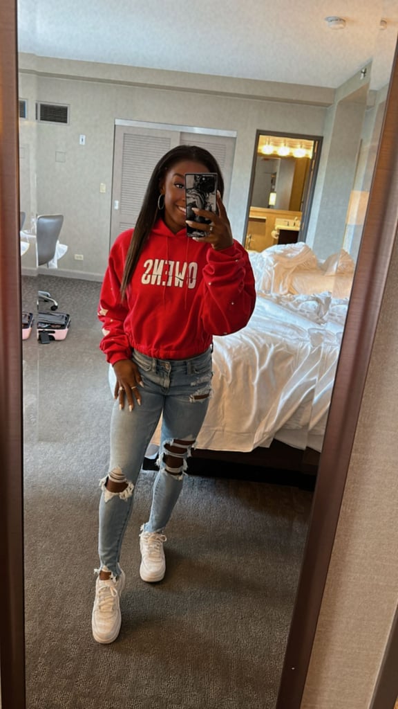 Simone Biles could teach any partner of a professional athlete a thing or two about dressing to show support. The 25-year-old Olympic gymnast has dedicated a whole section of her wardrobe to Houston Texans apparel, customized with fiancé Jonathan Owens's name and number. 
Her latest look is a cropped red hoodie that says "Owens" across the front in white block letters and embellished with round crystals on the sleeves. Biles teamed the design with ripped skinny jeans and white Nike sneakers for Sunday football, attending the Texans' game against the Bears in Chicago, IL. She shared an up-close glimpse of her accessories — black aviator sunglasses, her engagement ring, a couple of additional silver bands, and thin, silver hoop earrings — in a series of selfies posted to her Instagram Stories. "shots for breakfast send help," she wrote, informing her fans of the day's agenda. Biles, who opted for a natural, minimalist beauty look with her hair down straight, along with a milky white manicure, was more than prepared to cheer on her soon-to-be husband. 
It's not the first time she's shown off her outfits for various NFL events. Biles kicked off the season in a black onesie and shortly thereafter shared a sneak peek of herself in the Texans cheerleader uniform. On Aug. 14, she revealed a blue tie-dye tank top with "36" splashed across the front, Owens's jersey number.
This September, Biles also posted snaps from a DIY project in which she decorated clear PVC pouches with "Owens" and "36," making for the perfect personalized travel bags. But her silky, 2000s-inspired halter with glittery red embroidery, shared on Sept. 12 and styled with white denim cutoffs and coordinated sneakers, is likely most memorable. 
Ahead, see a few more angles of Biles's sweatshirt, and watch her feed to see which outfit tribute she posts next.

    Related:

            
            
                                    
                            

            Simone Biles Is Welcoming Fall in a Printed Turtleneck Minidress