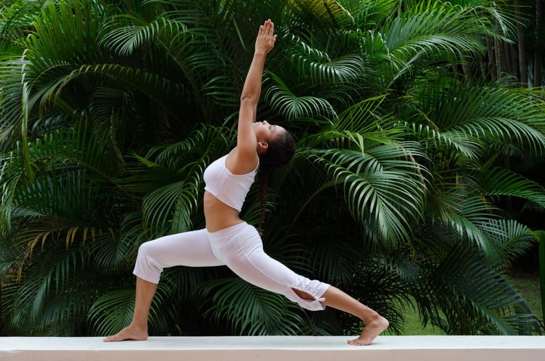 A woman doing a yoga pose on a garden (Ashwa Sanchalanasana)